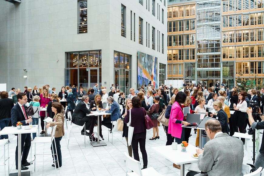 Menschen die an Tischen sitzen und stehen und miteinander sprechen