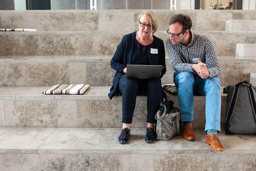 Eine Frau und ein Mann sitzen auf einer Treppe und schauen auf einen Laptop